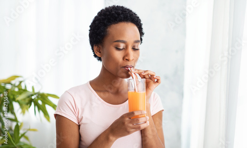 Fényképezés Pretty black woman drinking fresh orange juice at home, panorama