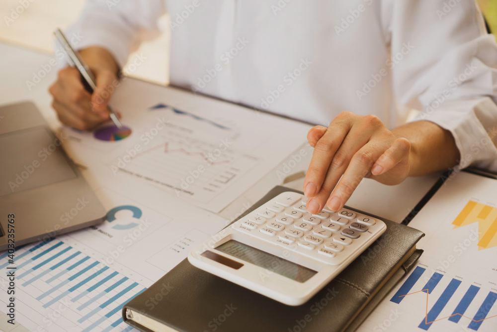 The female finance staff is calculating the company's profits from the graph on the home office desk. Concept finance The female finance staff is calculating the company's profits from the graph on the home office desk. Concept finance