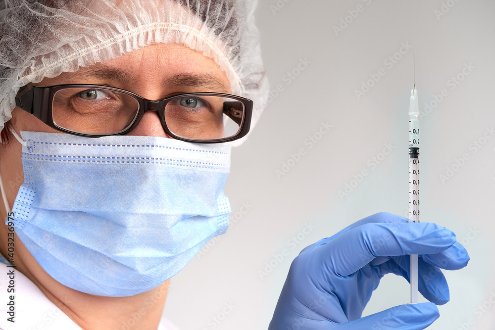 Coronavirus vaccine concept. Medic, doctor or nurse with covid-19 vaccine vial and syringe. Mature European female tech in face mask, glasses, disposable hat, gloves and protective white gown. Coronavirus vaccine concept. Medic, doctor or nurse with covid-19 vaccine vial and syringe. Mature European female tech in face mask, glasses, disposable hat, gloves and protective white gown.