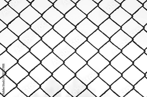 Black metal wire fence with rhombuses in park, view on white sky through it, camera in motion. Background, texture with metal grid and overcast sky in autumn day.