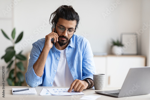 Young Arab Entrepreneur Talking On Cellphone And Working With Papers In Office