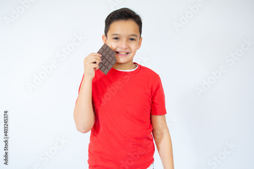 Little boy tries to taste a chocolate, look at the camera, in red T-shirt, isolated white background, copy space