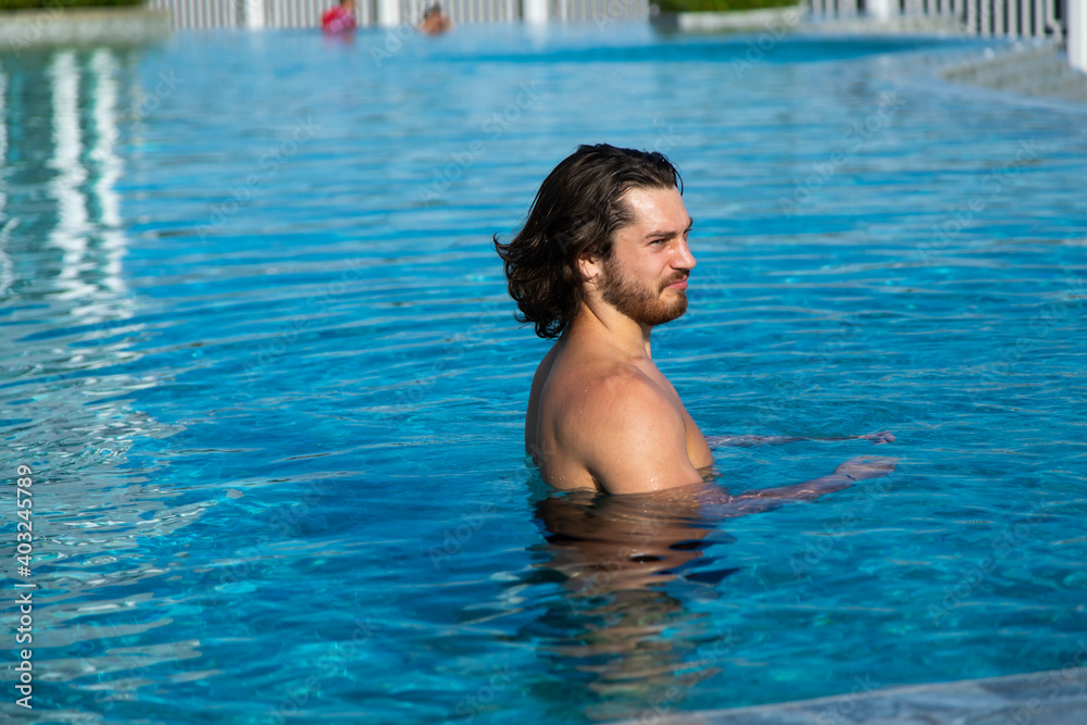 Portrait of a sexy handsome man resting at swimming pool. Summer vacation concept.