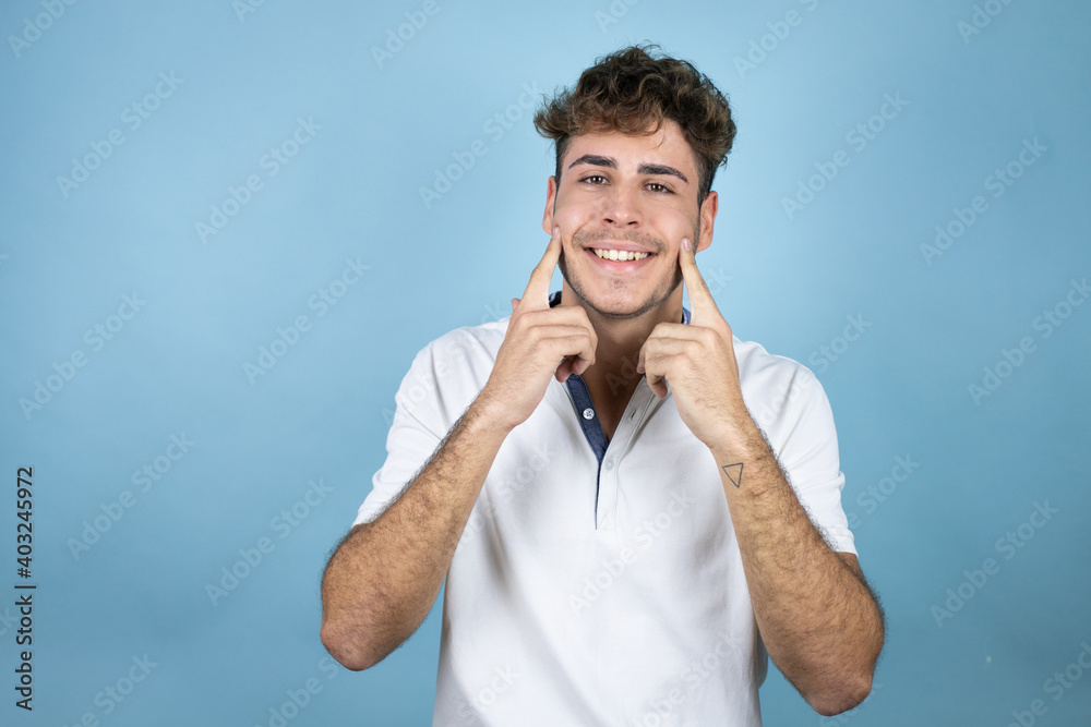 Young handsome man wearing a white t-shirt over blue background smiling confident showing and pointing with fingers teeth and mouth Young handsome man wearing a white t-shirt over blue background smiling confident showing and pointing with fingers teeth and mouth
