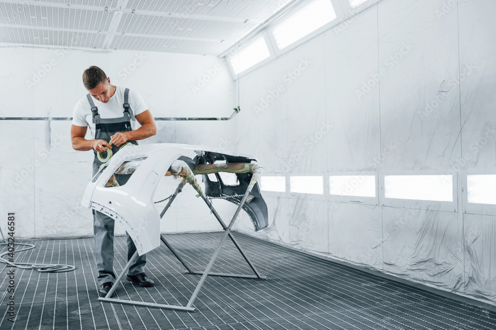 Fototapeta premium Works with car hood. Caucasian automobile repairman in uniform in garage