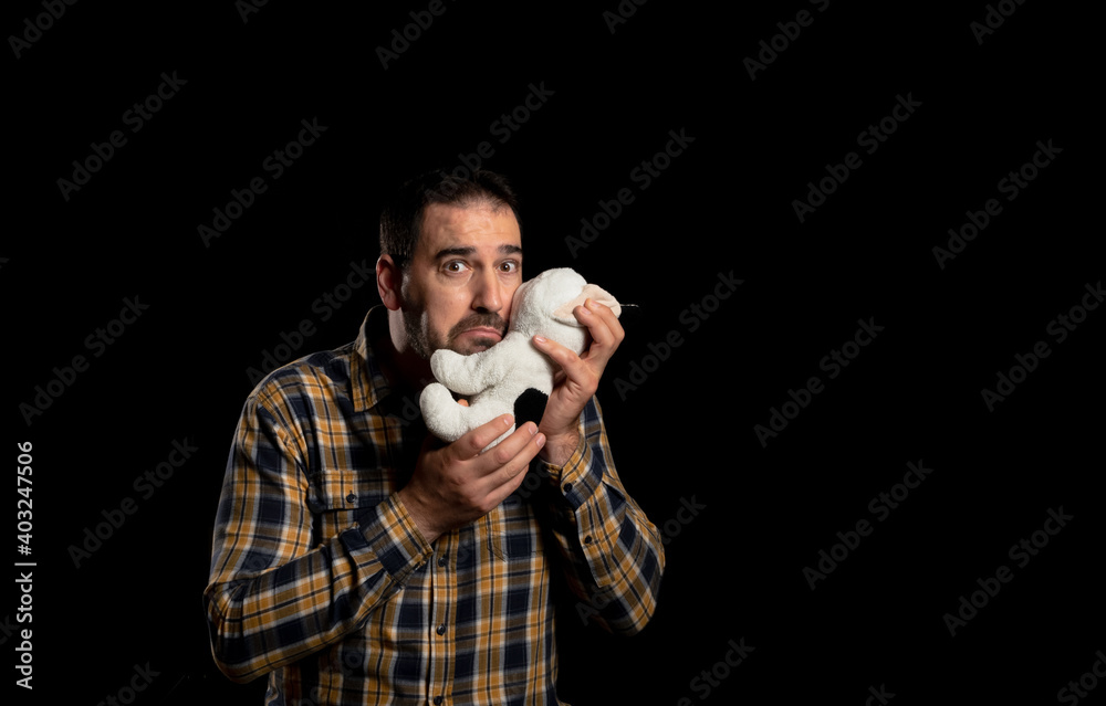 Attractive bearded man in a yellow plaid shirt with a stuffed puppy posing isolated on black background Attractive bearded man in a yellow plaid shirt with a stuffed puppy posing isolated on black background
