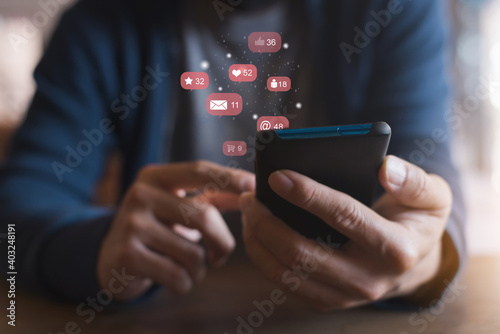 Fototapeta Naklejka Na Ścianę i Meble -  Man hand using a social media marketing concept on mobile phone with notification icons of like, message, comment and star above mobile phone screen.