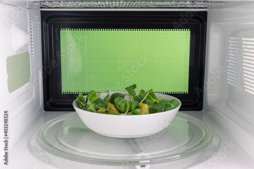 Young man heating food in the microwave. Green background for chroma key.