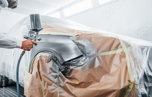 Painting job in progress. Caucasian automobile repairman in uniform works in garage