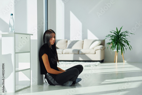 Young brunette in black clothes sits on the floor at home at daytime