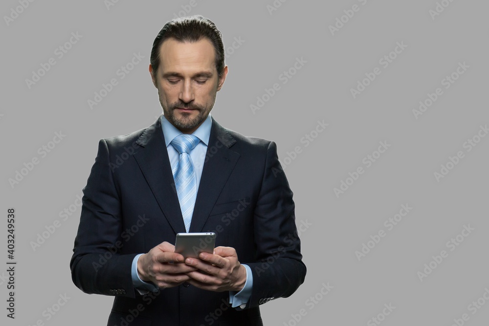 Attractive businessman using smartphone on gray background. Confident CEO using mobile phone. People, business and lifestyle concept. Attractive businessman using smartphone on gray background. Confident CEO using mobile phone. People, business and lifestyle concept.