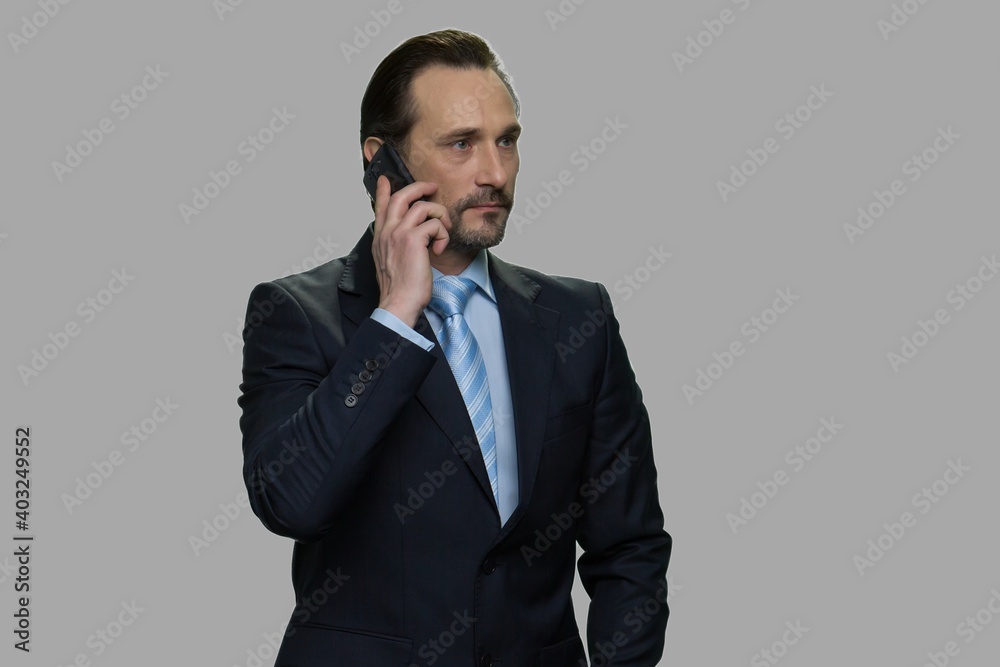 Successful businessman talking on cell phone. Confident male executive using smartphone on gray background. Concept of business conversation. Successful businessman talking on cell phone. Confident male executive using smartphone on gray background. Concept of business conversation.