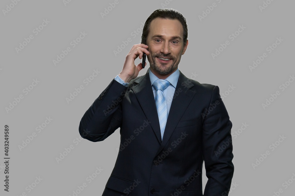 Smiling caucasian businessman talking on cell phone. Handsome male executive talks on mobile phone against gray background. Smiling caucasian businessman talking on cell phone. Handsome male executive talks on mobile phone against gray background.