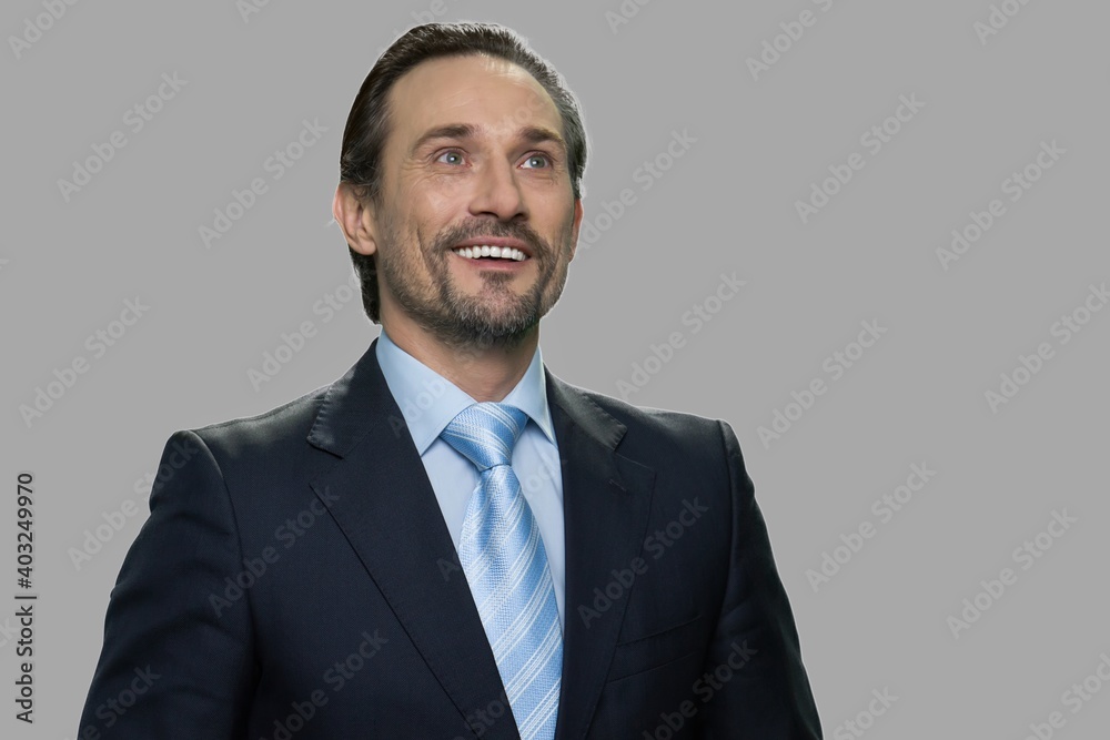 Happy smiling businessman with thoughtful expression. Attractive daydreaming business person on gray background. Dreaming about future success. Happy smiling businessman with thoughtful expression. Attractive daydreaming business person on gray background. Dreaming about future success.