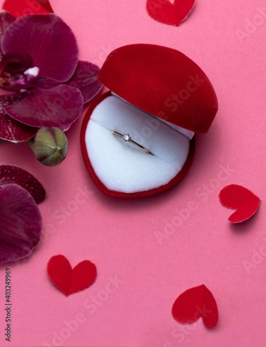 Wedding ring in a red box and red orchid on pink background. Valentine's Day. photo