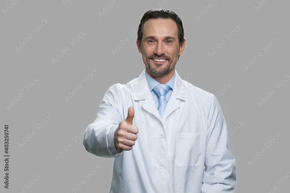 Happy doctor or scientist showing thumb up sign. Middle-aged man in white coat giving thumb up gesture against gray background. Good job concept. Happy doctor or scientist showing thumb up sign. Middle-aged man in white coat giving thumb up gesture against gray background. Good job concept.