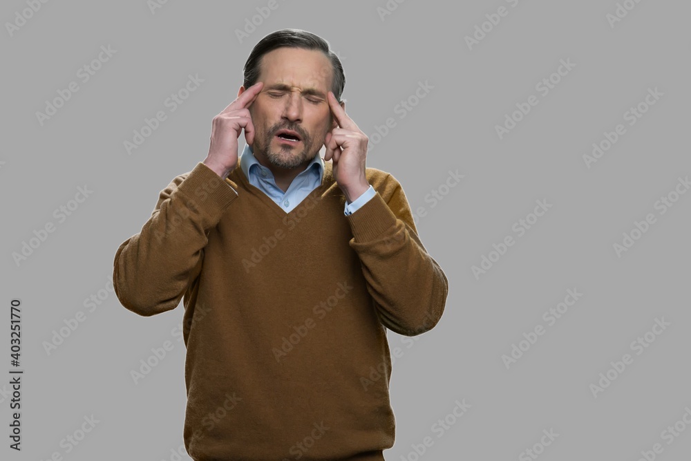 Man with terrible headache on gray background. Overworked man suffering from migraine. Fatigue and health problem concept. Man with terrible headache on gray background. Overworked man suffering from migraine. Fatigue and health problem concept.