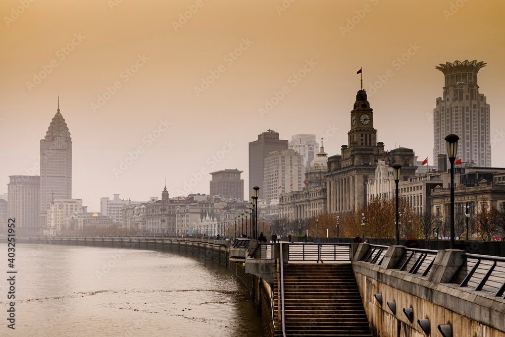 Historical architecture on the bund of Shanghai and modern city skyscrapers of Shanghai city skyline in misty gold lighting sunrise behind pollution haze, view from the bund in Shanghai, China.