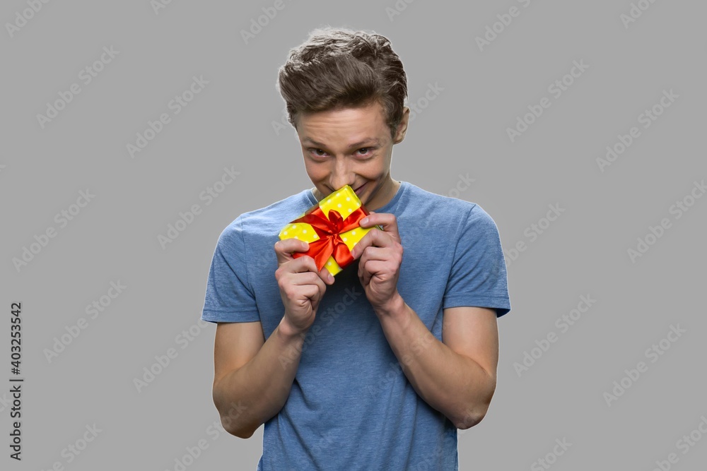Shy teen boy holding small gift box. Handsome teenage guy with present box standing on gray background. Shy teen boy holding small gift box. Handsome teenage guy with present box standing on gray background.