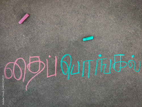 The inscription text on the grey board, "Thai pongal " in tamil letters. Using color chalk pieces.