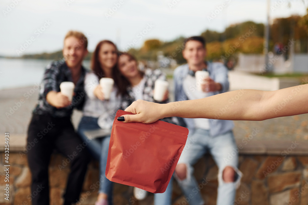Red package of coffee. Group of young cheerful friends that is outdoors having fun together