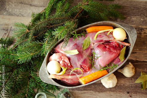 Roasted wild rabbit haunch with stewed vegetables in pan garnished with fresh herbs, top view