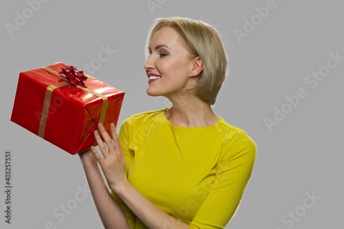 Happy woman looking at gift box in her hands. Pretty smiling girl holding present box on gray background. Gift for special event.