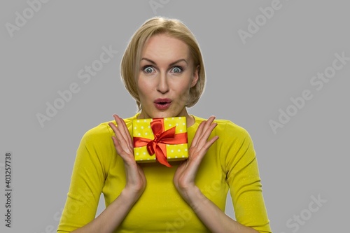 Close up happy shocked woman holding gift box. Young emotional woman holding present box on gray background. © DenisProduction.com