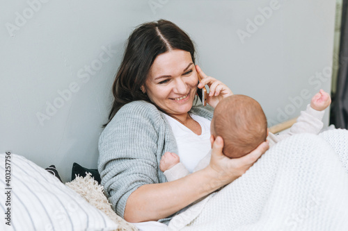 Mother speaking on mobile phone with cute baby boy on the bed, natural tones, love emotion