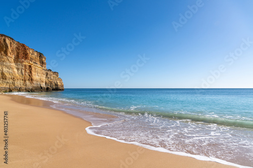 empty golden sand beach wth tropical turquoise water and rocky cliffs under a blue sky