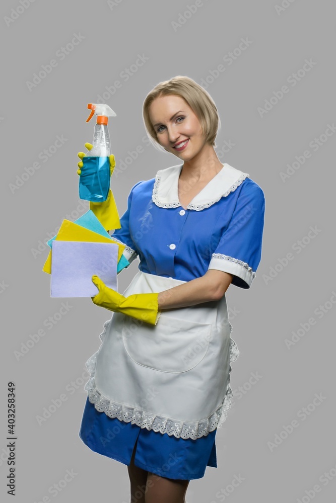 Attractive maid woman holding cleaner spray. Full length portrait of smiling cleaning woman showing rags and bottle of detergent. Attractive maid woman holding cleaner spray. Full length portrait of smiling cleaning woman showing rags and bottle of detergent.