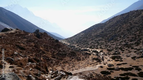 Trekkers and porters climbing up the trail to Dinboche, Khumbu, Nepal in the Himalayas on Everest Base Camp Trek with bright afternoon sun and sparse rock landscape. photo