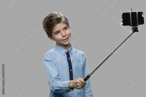 Funny boy using monopod on gray background. Handsome child taking photo with selfie stick. Kids, modern technology and fun.