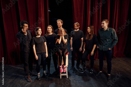 Girls sits on chair and crying. Group of actors in dark colored clothes on rehearsal in the theater