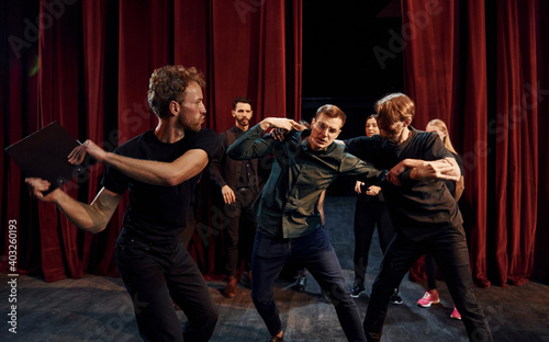 Fight scene. Group of actors in dark colored clothes on rehearsal in the theater