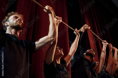 Holding rope in hands above the heads. Group of actors in dark colored clothes on rehearsal in the theater