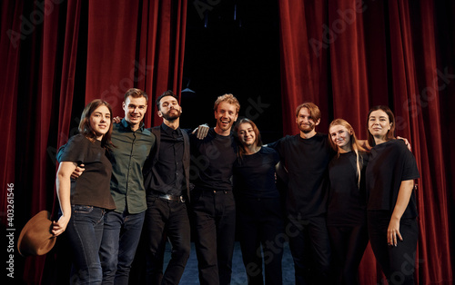 Standing against red curtains. Group of actors in dark colored clothes on rehearsal in the theater