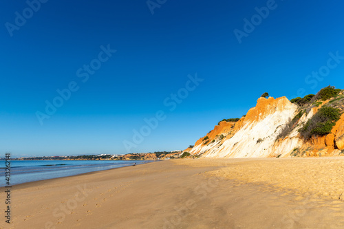 panorama view of a wide empty golden sand beach with colorful sand cliffs on a sunny day