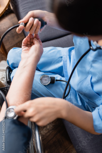 cropped view of nurse measuring blood pressure of senior woman with tonometer  blurred foreground