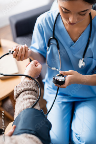 young asian woman measuring blood pressure of elderly woman with tonometer, blurred foreground