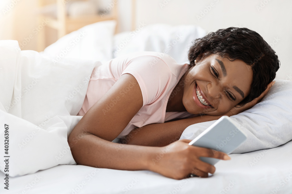 Happy young black woman using smartphone in bed Happy young black woman using smartphone in bed