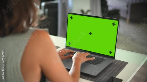 Woman typing on laptop with green screen mock up on table in bright room
