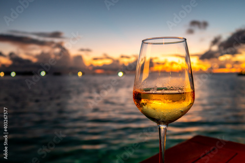 Glass of white wine on a table with dramatic sunset in the background and lights on horizon, Maldives. photo