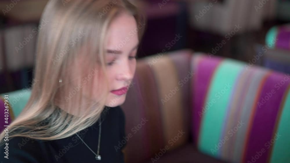 A gentle blonde woman in a restaurant glances to the side while sitting at a table. A gentle blonde woman in a restaurant glances to the side while sitting at a table.