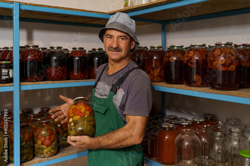 Man satisfied with the result of his work. He watches the shelves with marinated veggies in glass jares. Fermented organic food. photo