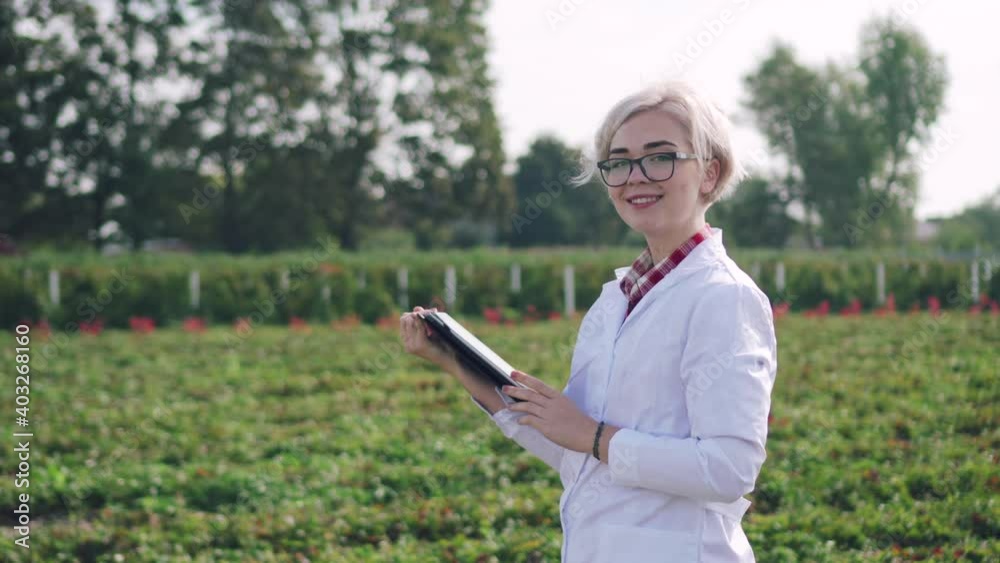 Agronomist at work. A young woman inspects the plants on the plantation and makes notes on the tablet. Agronomist at work. A young woman inspects the plants on the plantation and makes notes on the tablet.