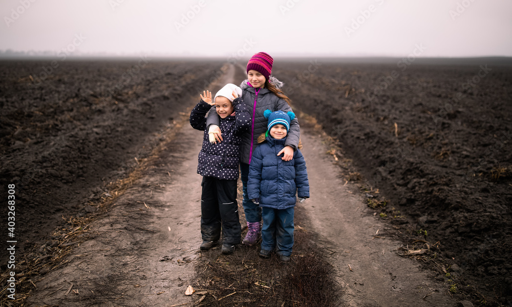 Three children (siblings) standing on road in the middle of Ukrainian broken field and smiling in winter