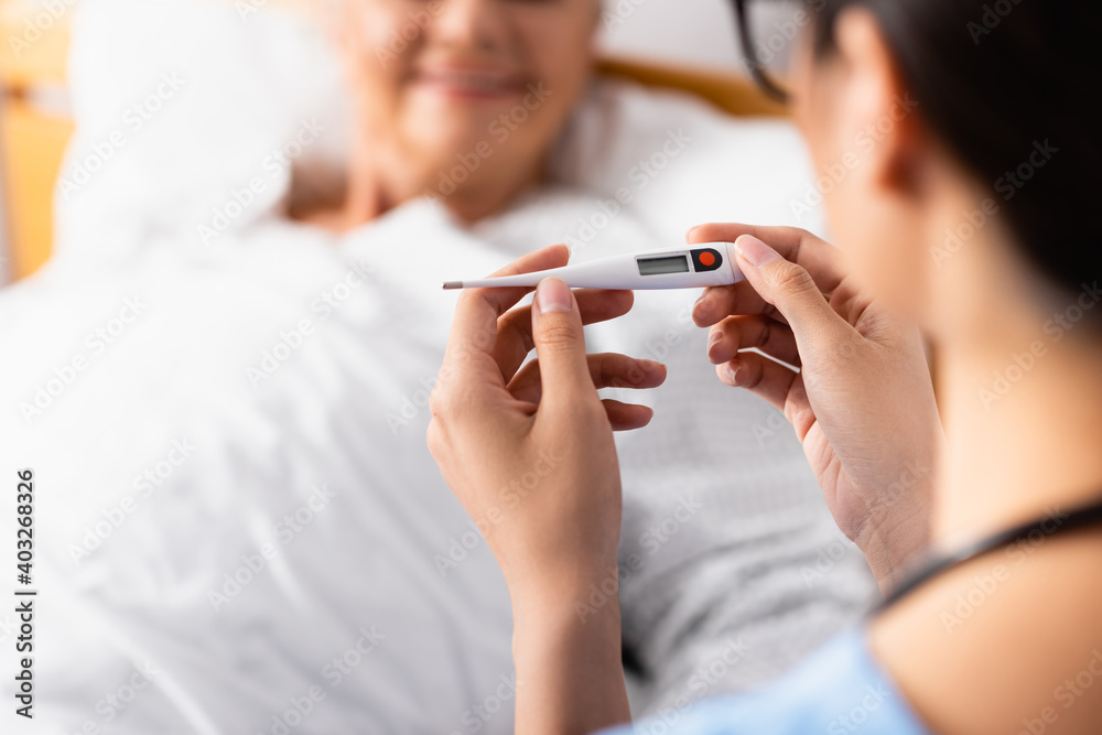 cropped view of nurse holding thermometer near aged patient on blurred background cropped view of nurse holding thermometer near aged patient on blurred background