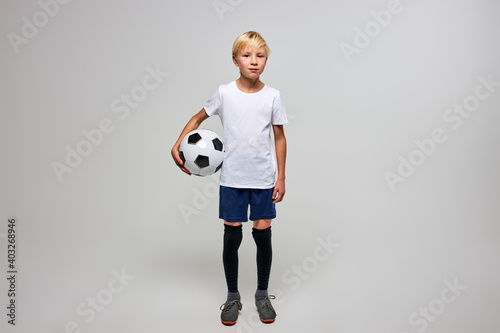 football player with ball isolated in studio, posing at camera, wearing football uniform, white t-shirt. sport, soccer concept © Roman