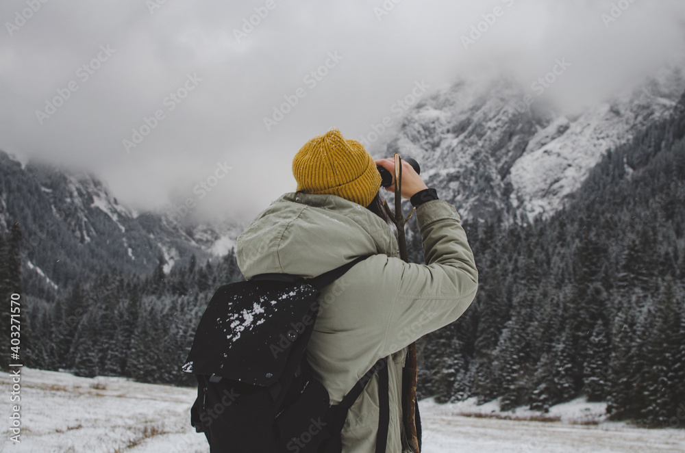 woman with backpack looking through binoculars, Winter foggy mountains. 